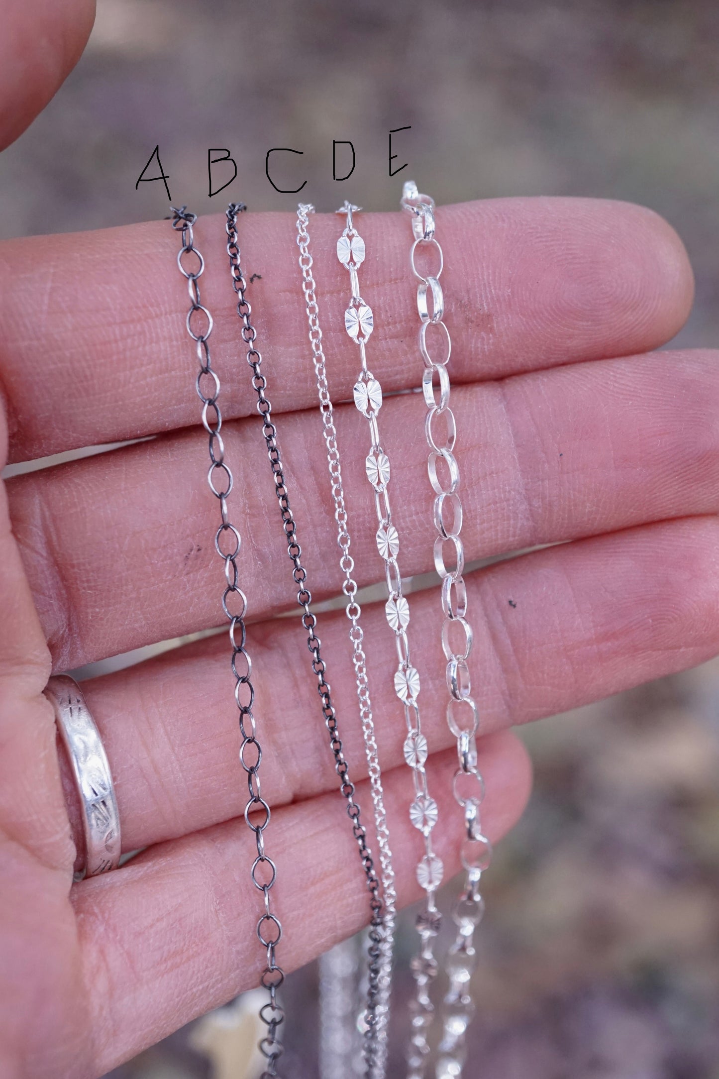 Close-up of a hand holding multiple silver necklace chains with a blurred natural background
