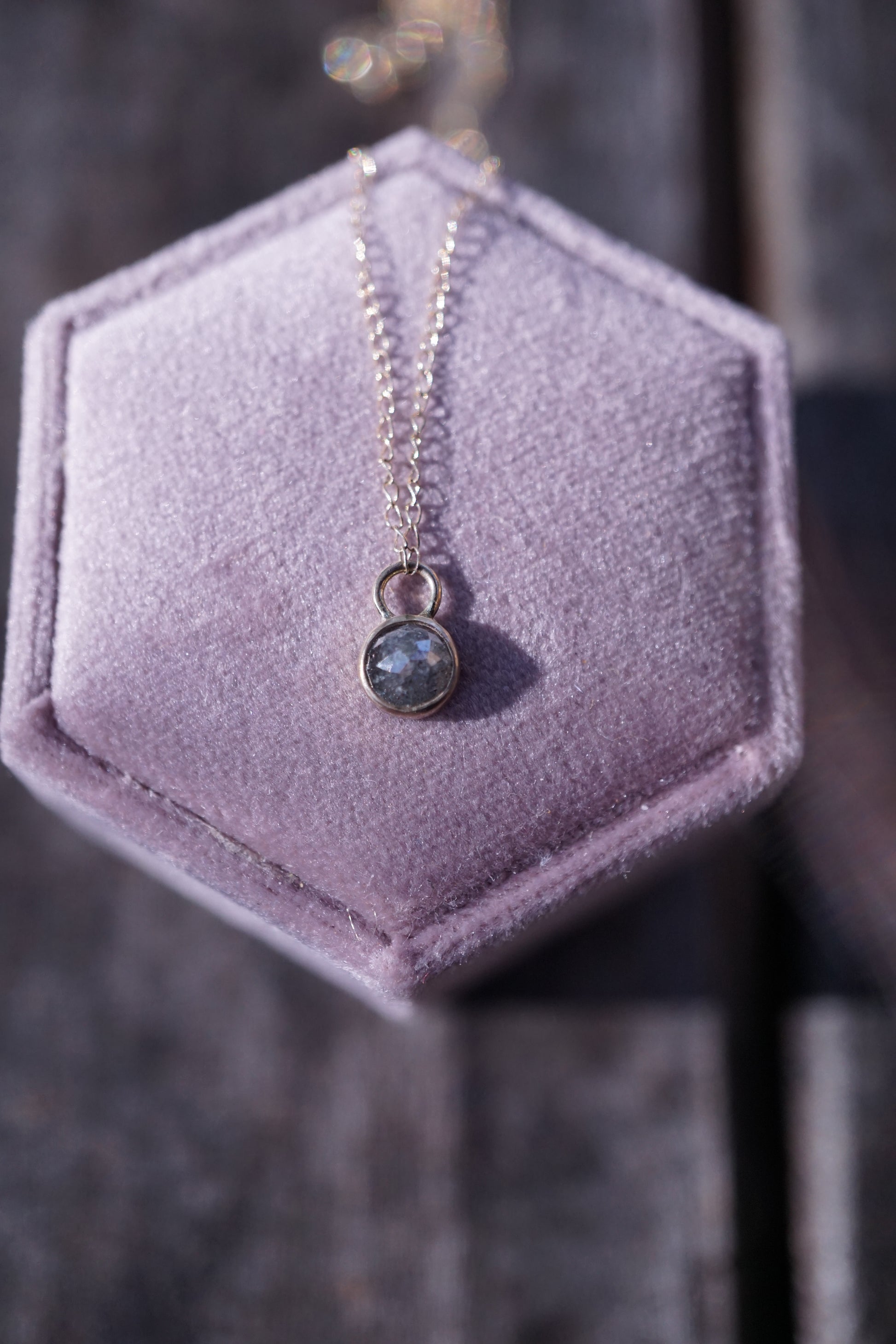 Gold Necklace with a diamond pendant on a hexagonal purple velvet stand