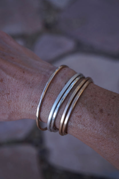Close-up of a wrist wearing multiple gold bracelets against a blurred natural background