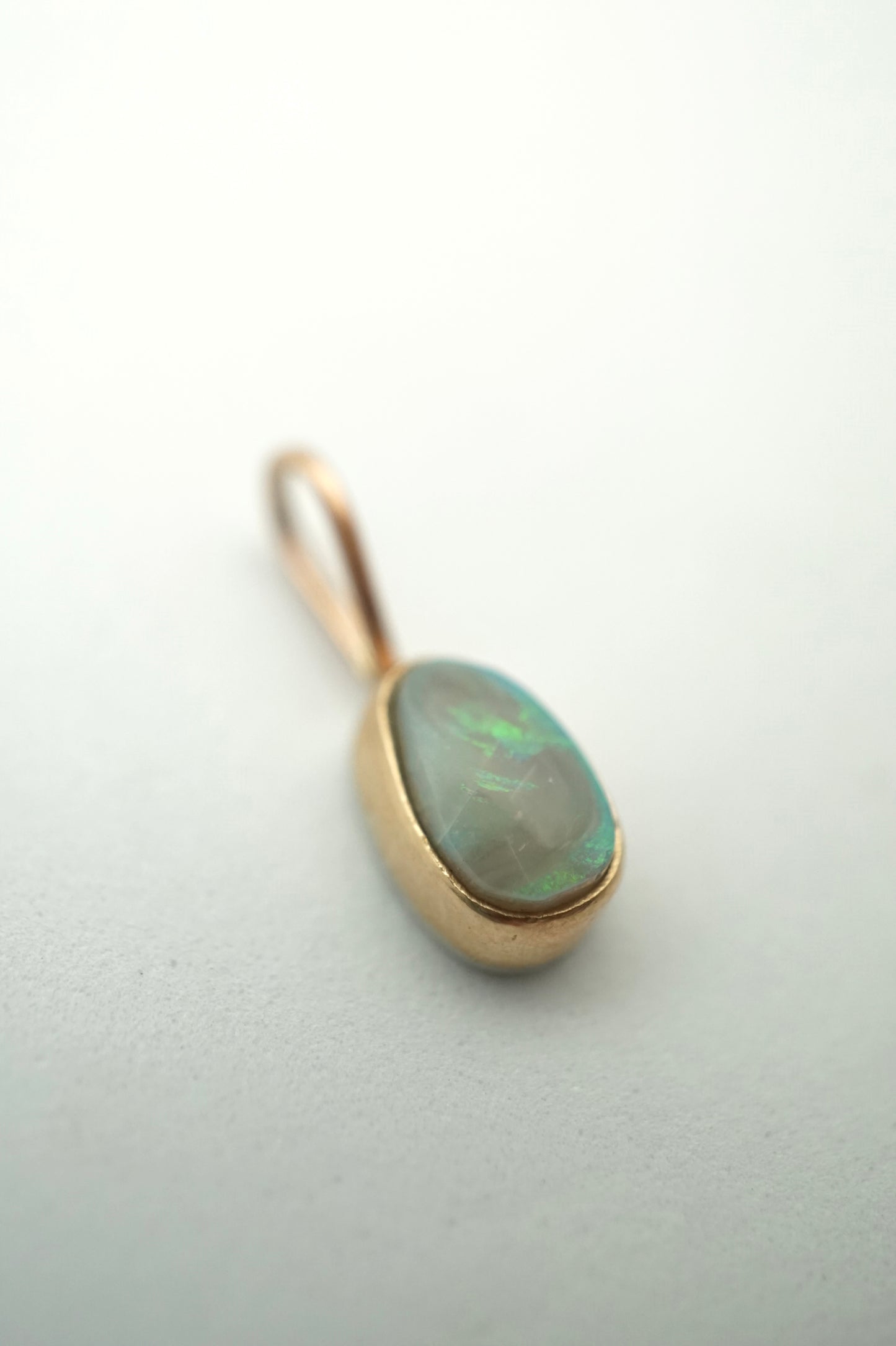 Gold pendant with an opal stone on a light gray background