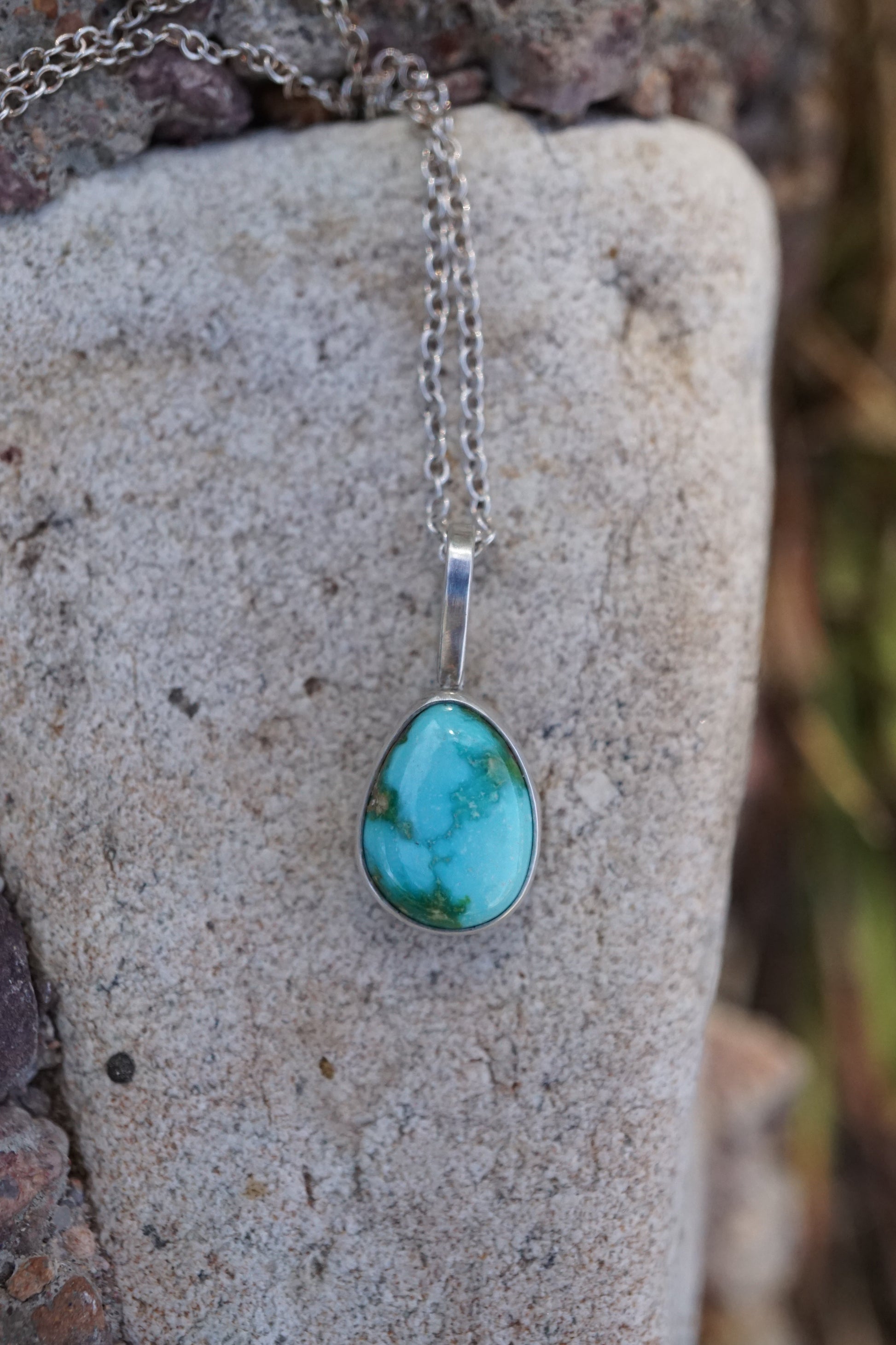 Turquoise pendant necklace on a stone surface with natural background